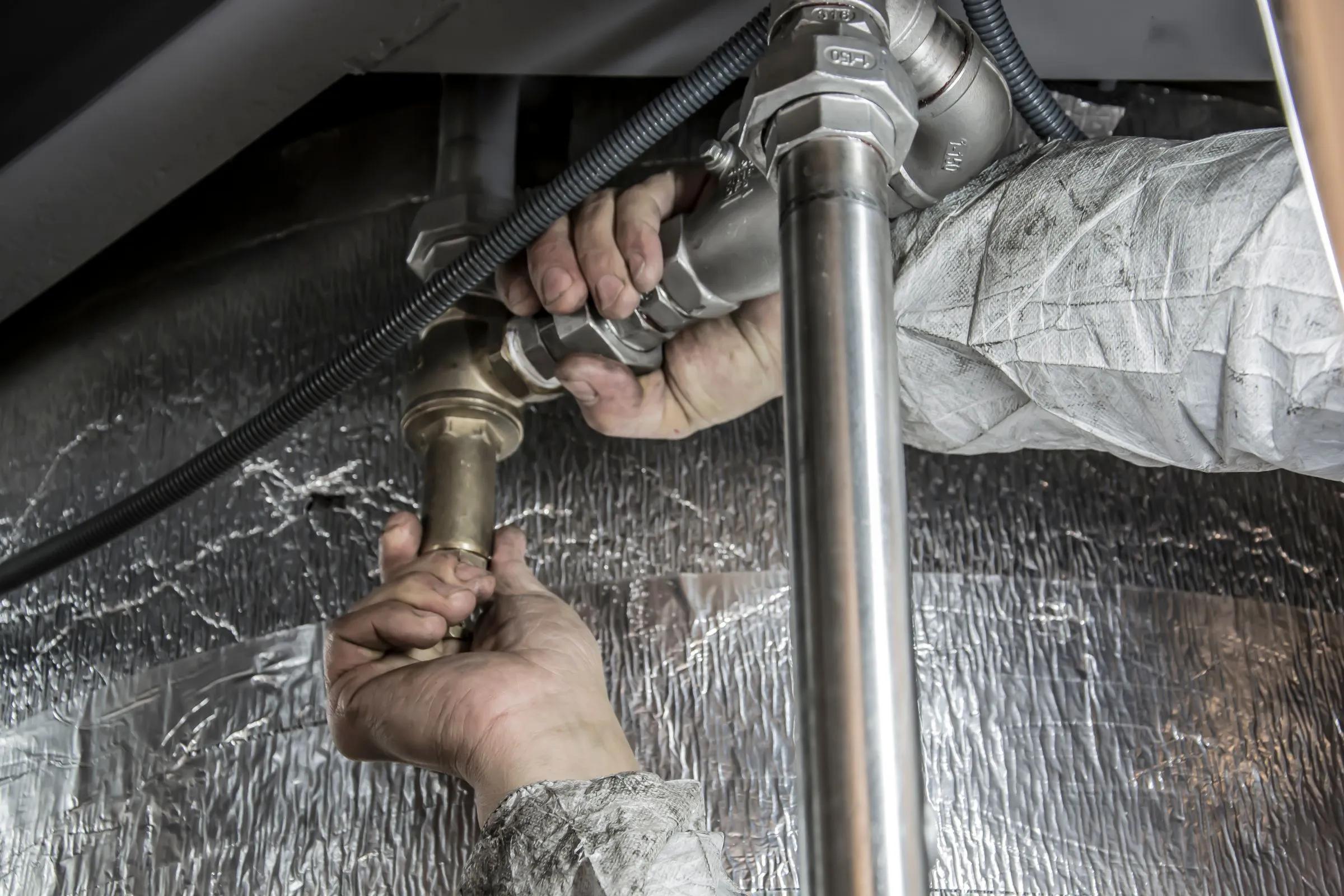 Maintenance worker repairing a plumbing pipe beneath a sink